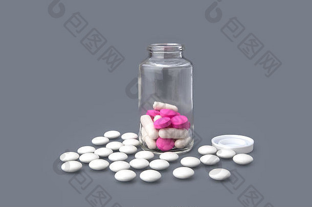 白色药片散落在一个玻璃瓶周围，灰色背景上有粉红色药片。