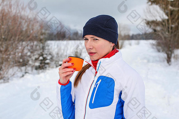 年轻的女人冬天体育运动夹克喝热<strong>茶</strong>橙色热水瓶瓶杯冷多云的一天雪覆盖景观背景