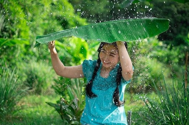 肖像年轻的亚洲女人黑色的头发持有香蕉叶下雨绿色花园背景