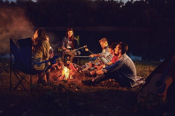 秋天夏天的晚上，一群人坐在帐篷旁的篝火旁。