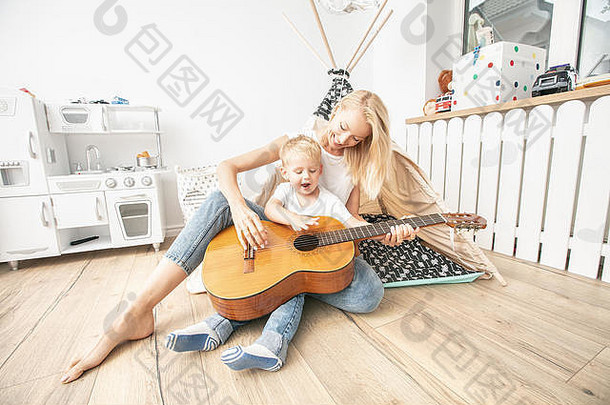 妈妈和小孩在孩子们的房间里玩耍。妈妈和儿子用吉他演奏音乐。在家的闲暇时间。家庭幸福和爱。