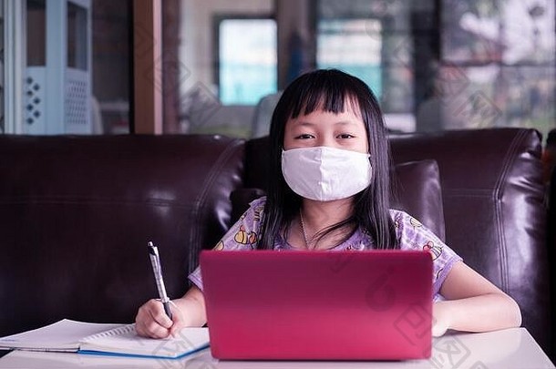 亚洲女孩在家里学习家庭作业，在网上上课时戴口罩，以保护2019年nCoV或新冠19病毒，在线教育c