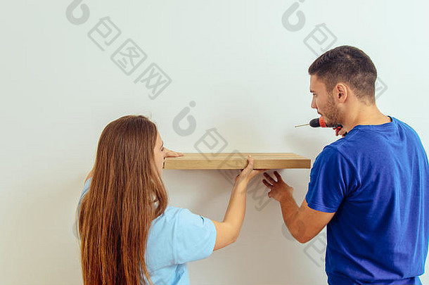一个年轻的工匠和他的女朋友用电钻在墙<strong>上架</strong>子的后视图