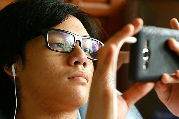 一位戴着眼镜和耳机的青少年在智能手机上观看视频的照片