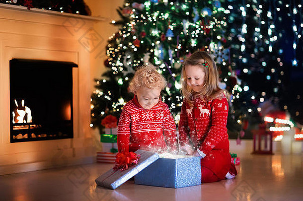 圣诞前夜，一家人在壁炉旁。孩子们打开圣诞礼物。孩子们在圣诞树下拿着礼物盒。