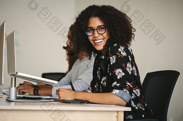 商务人士坐在办公室的工作站上。戴<strong>眼镜</strong>微笑的女商人坐在办公桌前，桌上放着笔记本电脑。