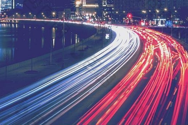 夜间，在莫斯科河堤岸附近，一辆带着模糊灯光的汽车穿过城市，照亮了Radisson或乌克兰酒店。莫斯科，俄罗斯。