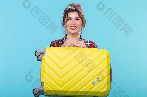 积极的年轻的微笑女人格子衬衫持有黄色的手提箱摆姿势蓝色的背景概念旅游旅行