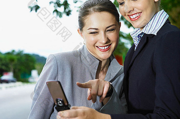 两位商务女士一边用手机一边微笑