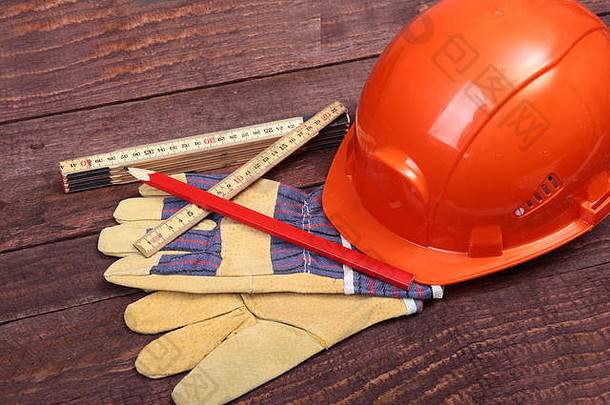 橙色安全帽和手套，用于在木质背景上工作。