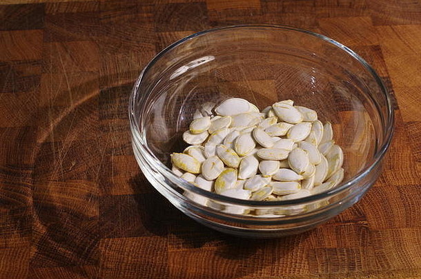 橡木砧板上一个玻璃碗的干南瓜籽的微距照片。健康饮食小吃。阿伯丁，苏格兰，英国。
