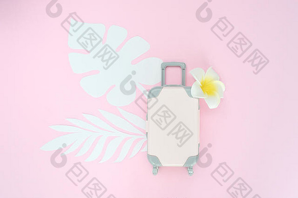 粉色旅行箱，粉色背景，热带树叶和白色花朵。旅游概念。平铺异国情调