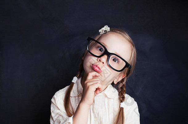 天真的儿童<strong>思维</strong>。有趣的小女孩戴着眼镜，背景是黑板，有复印空间。回到学校，孩子们的创造力和头脑风暴