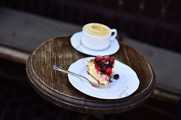 木桌上的芝士蛋糕配浆果和<strong>咖啡</strong>，特写。一块蛋糕，白杯子旁边有黑莓和覆盆子。美味的甜点，棕色<strong>纹理</strong>背景。糖果概念