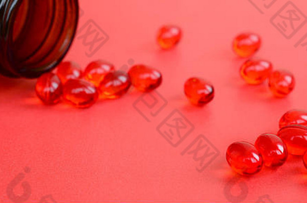 许多透明的红色药片散落在红色表面的一个棕色小玻璃罐中。