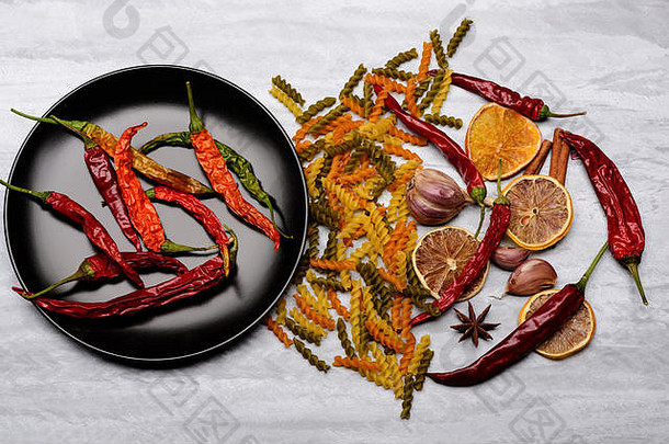 美味的五颜六色意大利面食辣椒，陶瓷黑色盘子，橙色，大蒜，八角和肉桂色，灰色纹理背景，俯视图