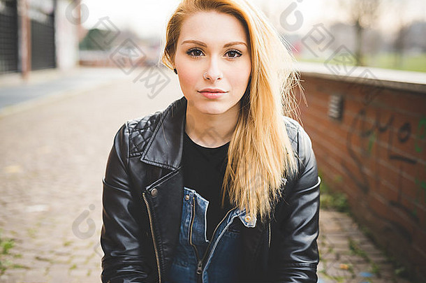 肖像年轻的美丽的金发女郎直头发女人城市相机沉思的穿黑色的皮革夹克