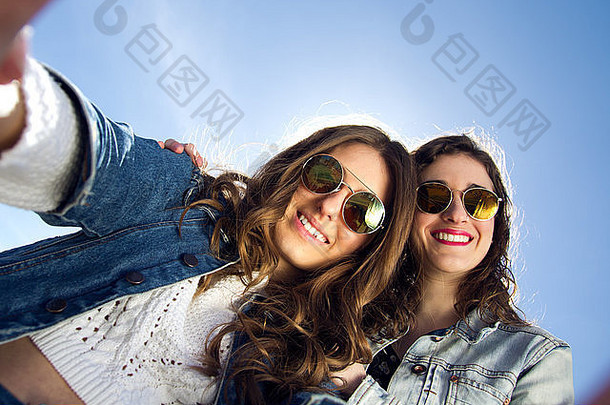 两个戴太阳镜的女孩用智能手机拍照