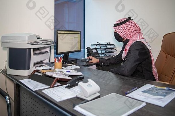 一名沙特男子戴着面具，在科罗纳大流行禁令开放后的第一个工作日在办公室工作