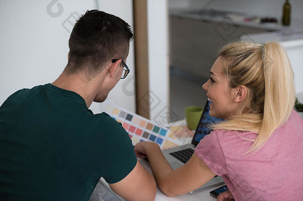 这对年轻夫妇搬进了新家。一男一女坐在桌旁使用笔记本电脑，并计划在他们周围放置盒子