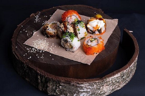 日本edp寿司卷放在木制托盘上，寿司卷上有金鱼、蔬菜和洒有芝麻籽的unagi酱汁