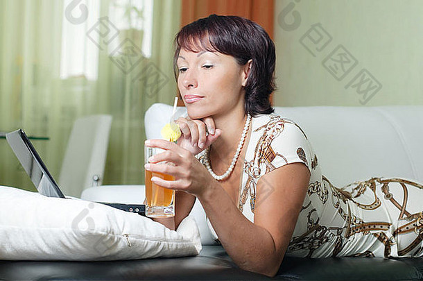 一位年轻女子躺在沙发上，写着笔记本，喝着果汁