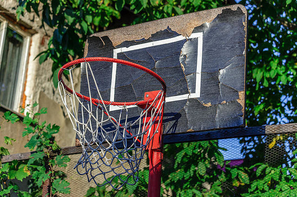 旧的和损坏的篮球圈，背景是笼子、树和房子，特写