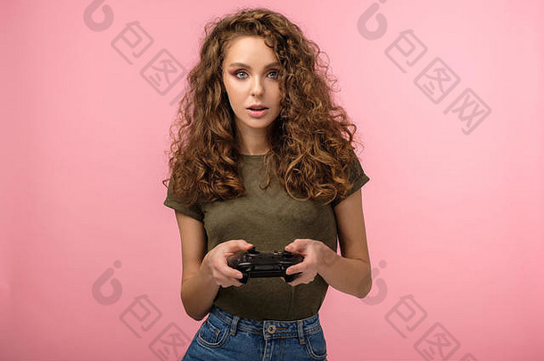 漂亮的游戏玩家女孩，卷发，手持游戏控制器，在粉色背景下表达一种惊讶的孤独感