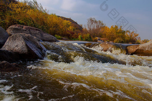 秋天，石头在湍急的河面上，黄色的树在岸边