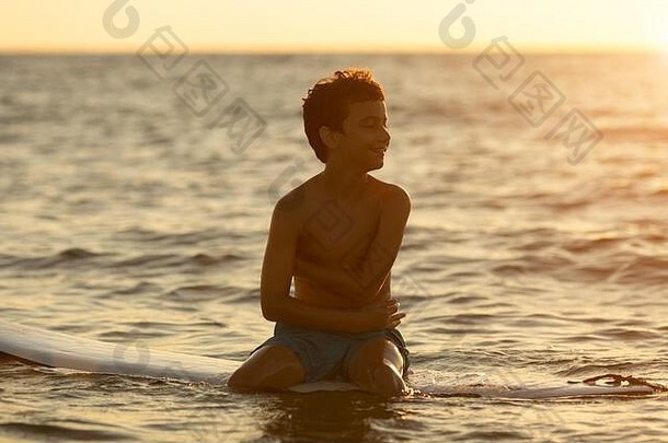 黎明时分，冲浪者坐在冲浪板上——男孩——穿着游泳短裤，在海滩上等待巨浪