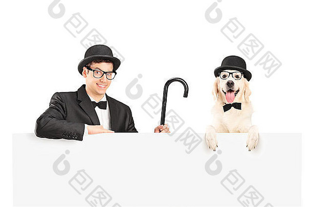 一个穿着西装，戴着复古帽子和手杖的表演者和一只狗在白色隔离板后面摆姿势