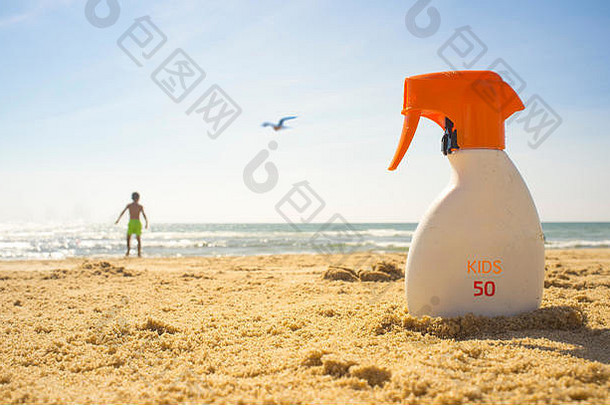 在沙滩上涂抹防晒系数为SPF 50的防晒霜。背景中的小男孩