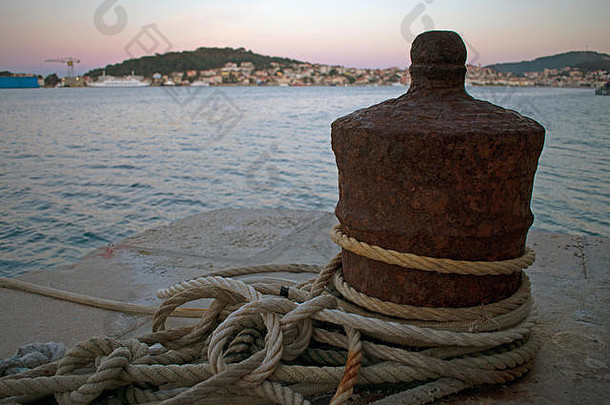 用绳索缠绕的生锈船只系泊特写镜头，背景为城镇