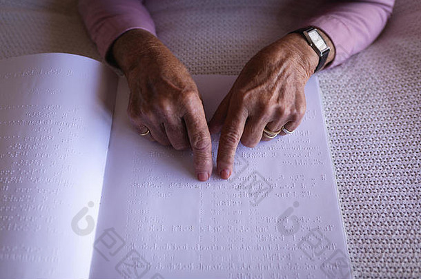 盲人活跃的老年妇女在家卧室的床上用手读盲文书