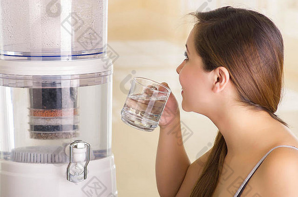 在厨房背景上，一位美丽的女士饮用一杯带有净水器过滤系统的水的特写镜头