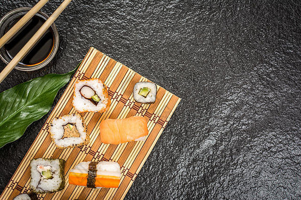 传统日本寿司卷hosomaki、uramaki、nigiri、筷子和酱油放在石头桌上俯视