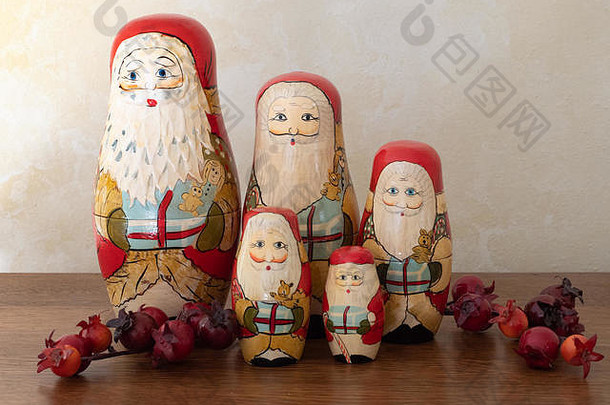 由五个手绘木制圣诞老人筑巢娃娃组成的小组，这些娃娃和红色浆果一起站在一起。