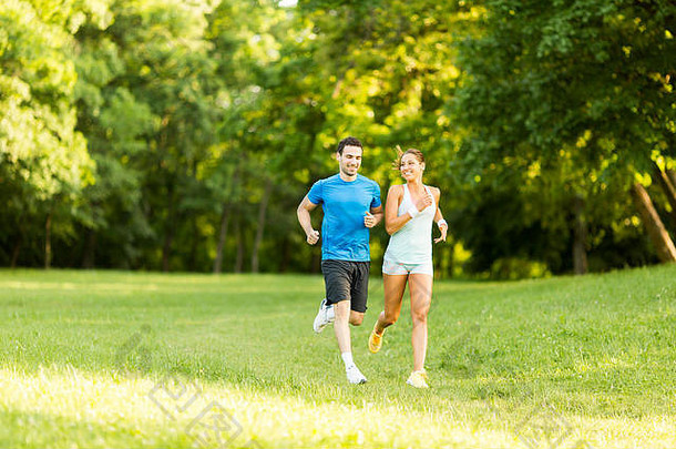 一对年轻夫妇在阳光明媚的日子里在公园里跑步
