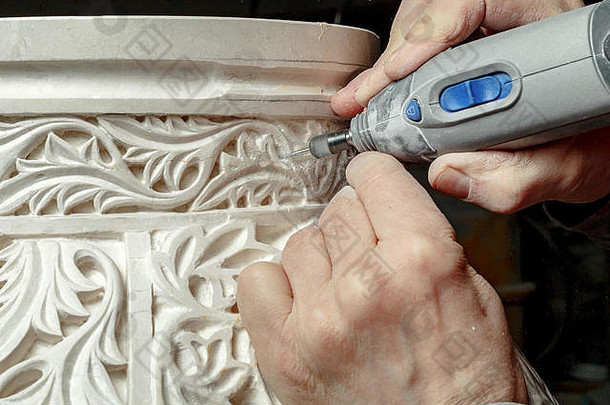 无法辨认的工匠用电动工具在灰泥表面雕刻花卉装饰的特写手