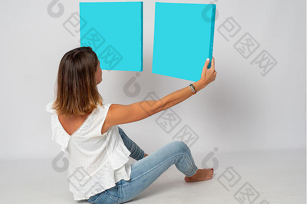 金发女孩坐在白色背景的地板上，拿着蓝色的图片来放你的文字