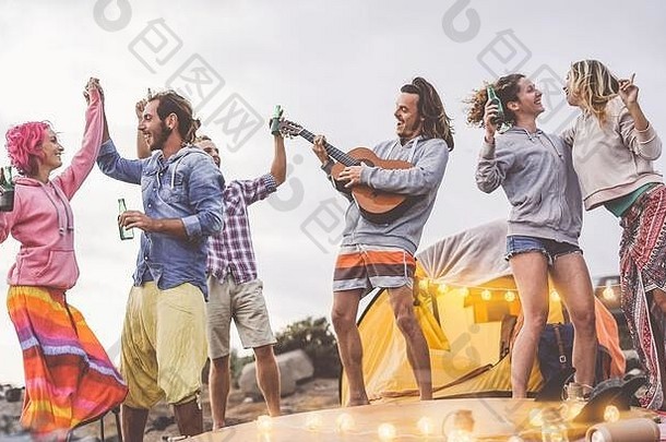 一群朋友在聚会上弹吉他，在户外野营——快乐的年轻人在营地里喝啤酒，欢笑
