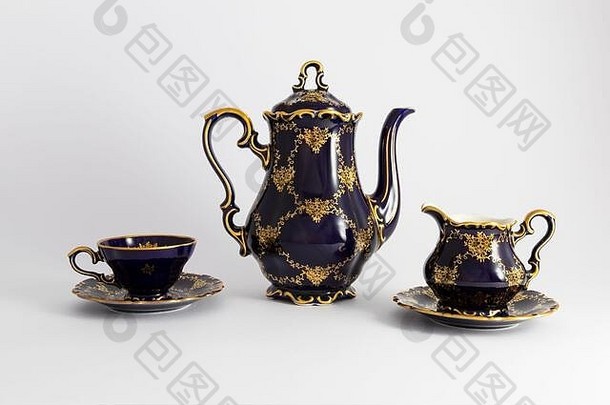 一套美丽的钴蓝色复古瓷<strong>茶具</strong>的特写镜头，白色背景上有金色<strong>花</strong>朵图案。这套包括一个茶壶，一个茶壶