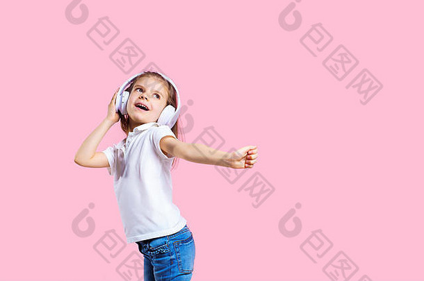 戴着<strong>粉色</strong>背景耳机听音乐的女孩。可爱的孩子享受着快乐的舞蹈音乐，微笑着，在<strong>粉色</strong>工作室的背景<strong>墙</strong>上摆姿势。