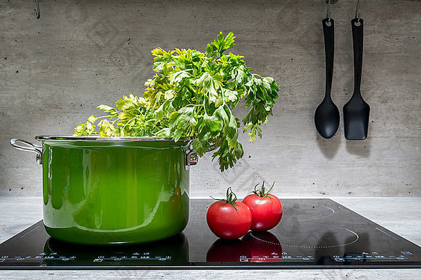 绿色搪瓷炖锅，配欧芹和两个西红柿，放在黑色电磁炉上