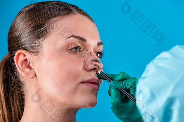 美容师在女人脸上画矫正线。在整形手术之前。蓝色孤立