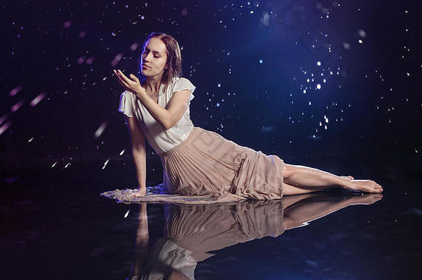 摄影艺术，年轻女子梦想星空。年轻漂亮的黑发女郎坐在水面上，看着星星。