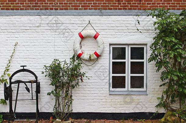 红白相间的砖墙，带窗户、绿色灌木丛、红白相间的救生圈和黑色历史锚绞车