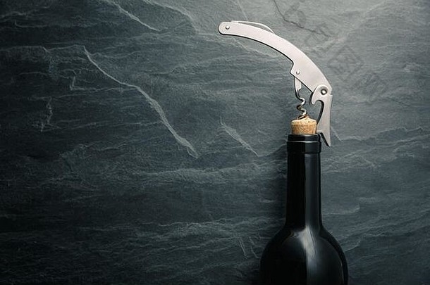 在黑色岩石板岩背景上的葡萄酒瓶口软木塞上的不锈钢葡萄酒瓶塞螺丝