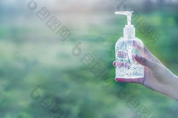 手拿透明白色塑料瓶抗菌消毒剂液，背景为绿色，复印空间清晰