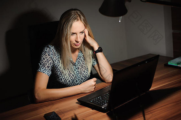 一幅女商人坐在办公桌前思考解决方案的照片，她在电脑前工作到很晚。